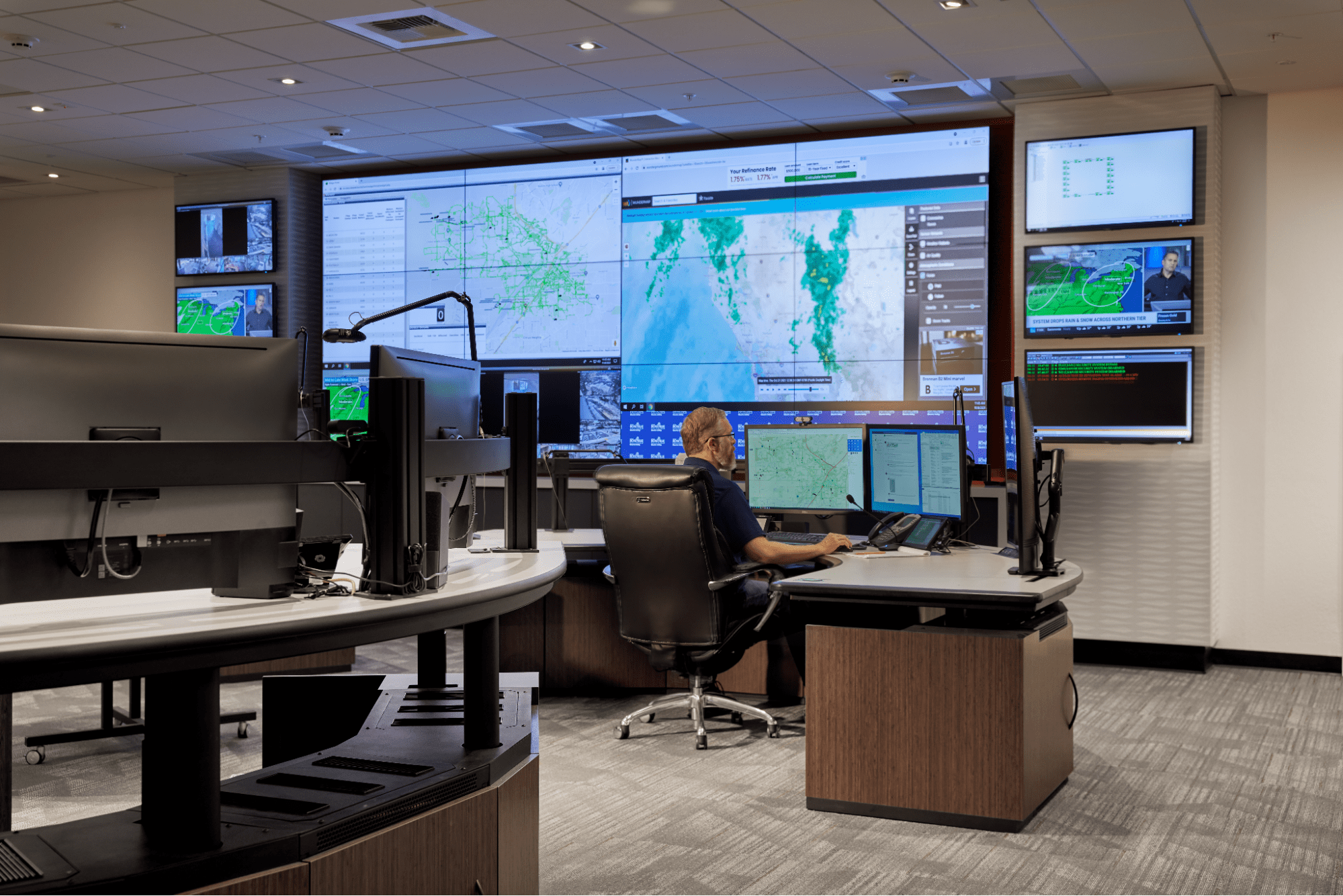 A controller sitting in a control room with a computer and a video wall