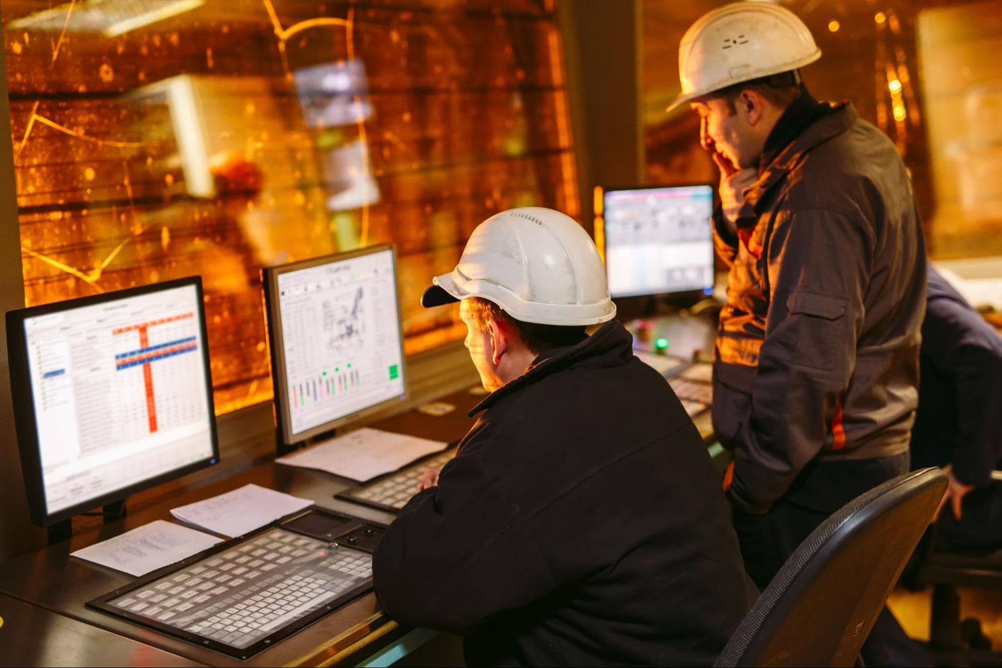 two control room operators analyzing charts on computer screens.